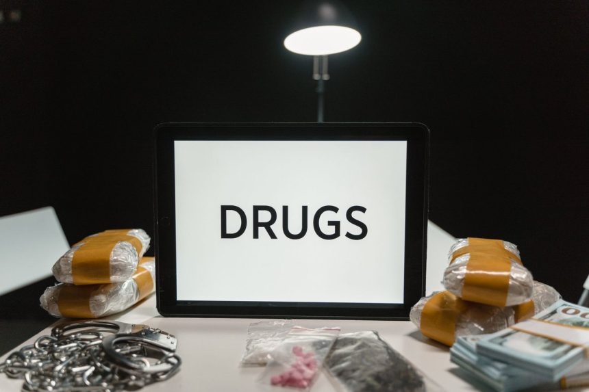 Drogas, dinheiro e algemas sobre uma mesa sob iluminação intensa.