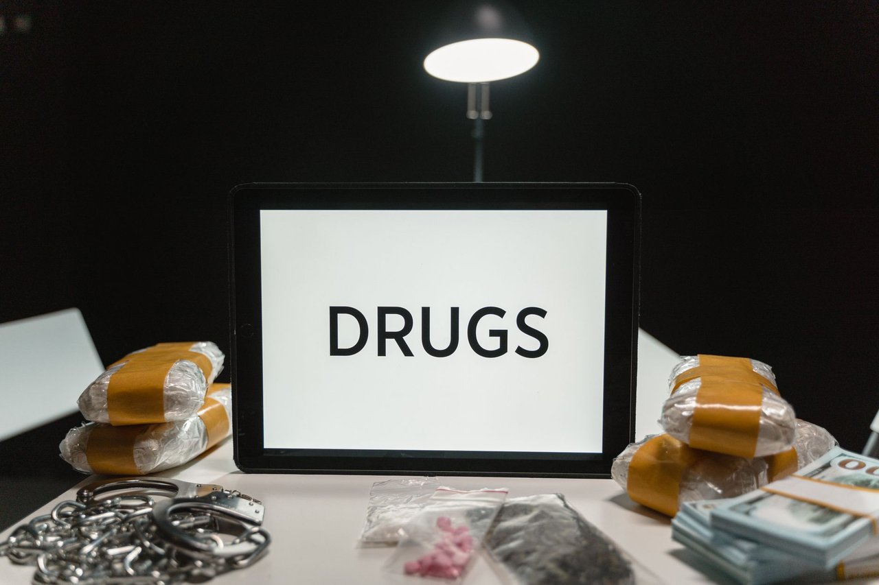 Drogas, dinheiro e algemas sobre uma mesa sob iluminação intensa.