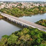 Vista aérea de uma ponte sobre um rio, cercada por vegetação.