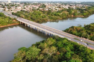 Vista aérea de uma ponte sobre um rio, cercada por vegetação.