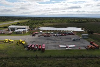 Vista aérea de uma base de combate a incêndios com aviões, caminhões e equipes de emergência reunidos.